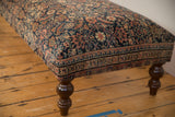Persian Fereghan rug ottoman: tailored corner, navy and coral pattern, dark turned leg.