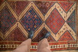 A person's overhead view of the antique Hamadan rug's rich texture and stepped geometric medallions.