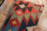 Vibrant flatweave geometric pattern in coral, sage, and dark tones on a vintage pillow.
