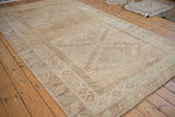 Distressed vintage Kars carpet showing geometric border and abrashes field in muted beige and pale green.