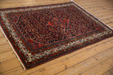 Vintage Persian Hamadan rug from an angle, showing the navy field and red geometric Herati pattern.