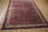 Vintage Hamadan rug with a navy Herati field and red medallion, viewed from an angle.