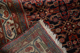 A vintage Hamadan rug corner folded back to reveal its hand-knotted construction and fringe.
