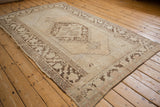Distressed Oushak rug corner highlights worn pile, ivory field, and rich brown patterns.