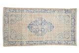 Distressed vintage Oushak rug with a cobalt blue shield medallion on a worn cream and ivory field.