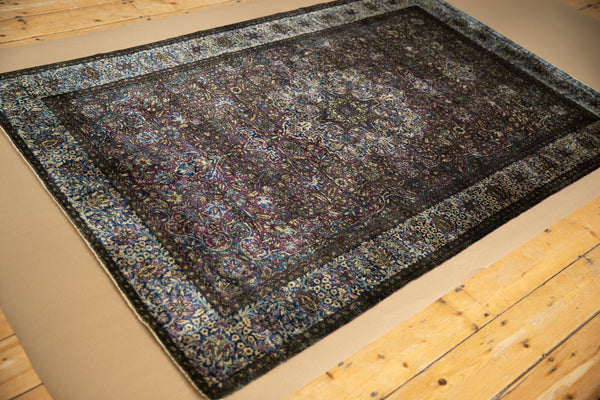 The dark side of an antique silk Kashan rug showing deep violet and blue floral patterns.