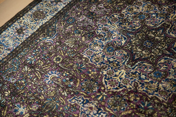 Close-up detail of the worn silk pile on an antique Kashan rug in deep purple, blue, and gold.