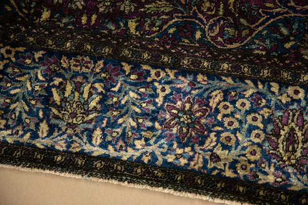 Corner of an antique silk Kashan rug showing the blue, violet, and gold floral border.