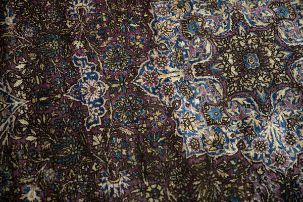 Close-up of the antique silk Kashan rug showing areas of wear and a recessed pile in deep purple and blue tones.