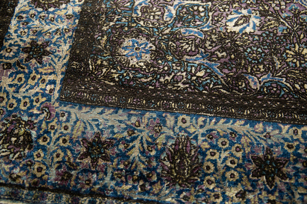 Close-up of the worn silk pile and detailed floral border in shades of blue and violet.