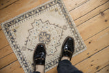 A small distressed Oushak rug mat with a geometric pattern, shown for scale underfoot.