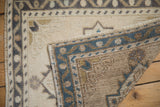 Folded corner of a distressed Oushak rug showing the hand-knotted reverse and machine-bound edge.