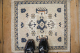 Distressed vintage Oushak square mat with ivory field, navy blue central blossom, wave border.