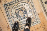 Distressed vintage Oushak rug corner with v-shaped leaf motifs and beige, navy tones.
