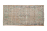 Distressed vintage Oushak rug runner featuring faded floral medallion, beige, green, and blush tones.
