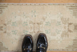 Distressed Oushak rug detail with worn cream pile and muted pale jade green floral patterns.