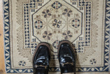 Distressed Oushak rug detail showing cream, dusty navy, and copper pomegranate motifs.