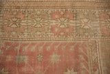 Distressed vintage Oushak rug border detail with pink, ivory, and sage geometric hook and latch pattern.