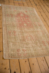 Distressed Oushak rug with faded pink, sage geometric patterns and exposed foundation.