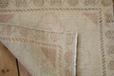 Distressed vintage Oushak rug detail with muted cream, dusty rose pile and machine-bound edge.