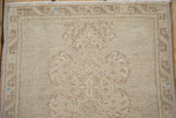 Distressed beige Oushak rug's low pile, showing faded geometric motifs and subtle blue accents.