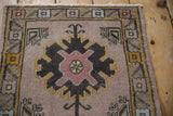 Distressed Oushak rug featuring a mauvish pink field, charcoal palmette, and geometric gold border.