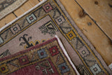 Folded distressed Oushak rug revealing a mauve field, geometric border, and dark red patterned underside.