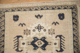 Corner view of the Oushak mat's wave border in dusty navy and beige on a low, evenly worn pile.
