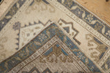 Distressed Oushak rug corner showing worn beige, blue patterns and machine-bound edge.