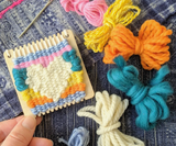 Lil Loom Weaving Kit displaying bright yarns, a woven heart, and tapestry needle.