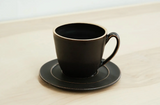 Black matte ceramic mug and saucer, handmade with natural edge details.