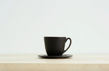 Black matte ceramic mug and saucer, side view with bronze-edged handle.