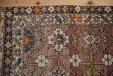 Abrash mauve field of antique Caucasian rug with geometric ivory, tangerine, and sky blue patterns.
