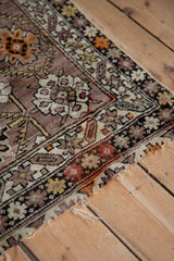 Angled close-up of antique Caucasian rug's tattered end, showing geometric vines and mauve ground.