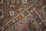 Mauve-ground antique Caucasian rug detail with geometric-floral patterns, folded to show woven structure.