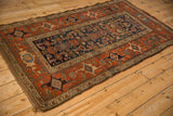 Angled view of an antique Kurdish Hamadan rug with a terracotta Samovar border and navy Herati design field.