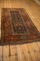 Angled view of an antique Kurdish Hamadan rug, showing its navy Herati field and terracotta border.