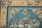 Corner of an antique Peking rug showing the blue field, arabesque border, and wear to the foundation.