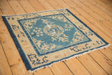Antique Peking square rug shown from an angle, highlighting its worn texture and sky blue field.