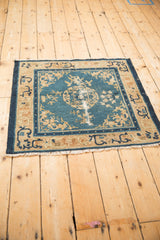 Angled view of the square antique Peking rug, highlighting its storied character and blue field.