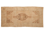 Distressed vintage Oushak runner, beige field with scalloped floral medallion in dusty red and bronze.