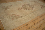 Distressed Oushak rug end corner, beige field, faded bronze spandrel, and machine finished edge.