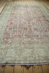 Distressed texture of vintage Sparta rug, faded raspberry thousand flower motif, arabesque border.