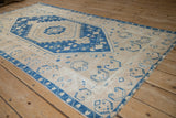 Angled view of a distressed Oushak rug's sapphire blue medallion and geometric patterns on a beige field.