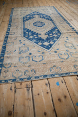 Low-angle view along a distressed Oushak runner showing its blue geometric pattern on a sand-colored field.