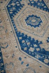 Low, hand-knotted pile of a distressed Oushak rug with geometric blue and sand starburst patterns.