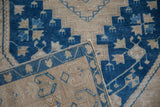 A folded corner on a vintage Oushak rug reveals the hand-knotted texture of its sapphire blue and sand geometric patterns.