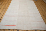 Hand-bound end of a vintage hemp kilim showing the plain-weave texture and a cantaloupe stripe.