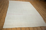 Angled view of the hand-woven hemp kilim showing its ivory texture and a thin pink stripe.