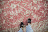 Distressed vintage Oushak rug with faded cochineal red field and ivory floral border.